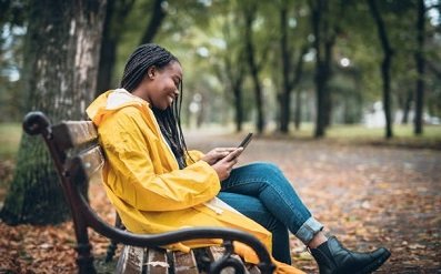 Young woman with yellow raincoat enjoying in the autumn park, using digital tablet