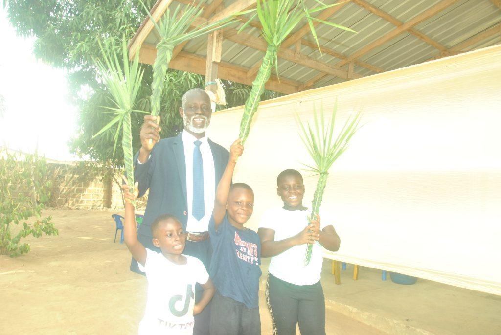 Mr Emmanuel Akpor Sowah with some children [From] Presbyterian Church of Ghana Kpobiman holding palm branchers