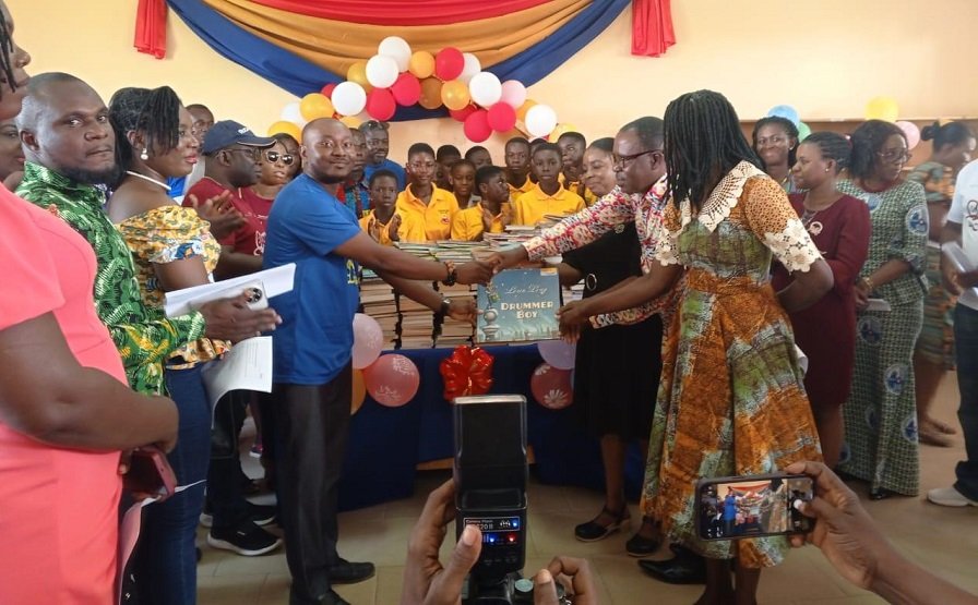Mr Afetor handing a book to the head of beneficiary school