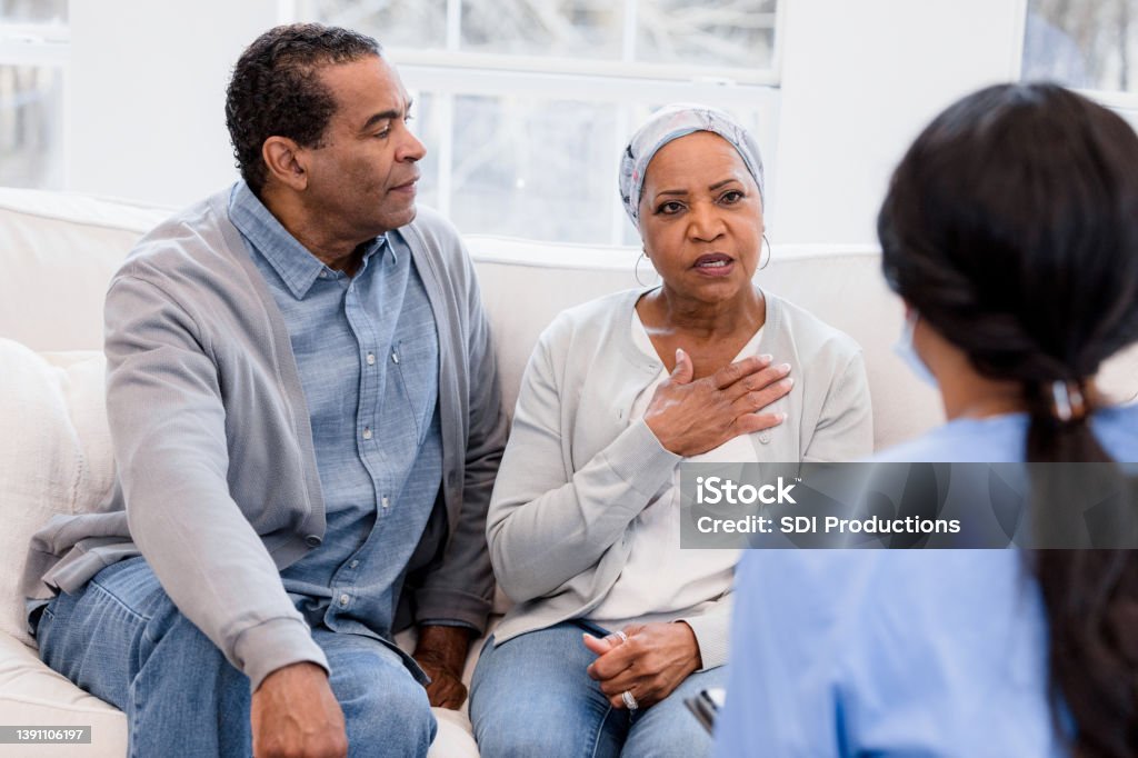 The senior woman holds her chest and talks to the nurse to describe the pain she has been having.