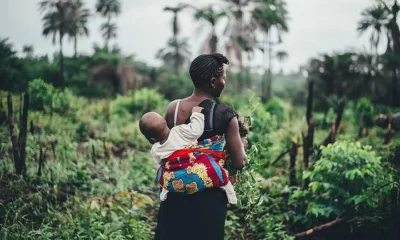 A woman farming with a baby strapped at the back