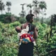 A woman farming with a baby strapped at the back