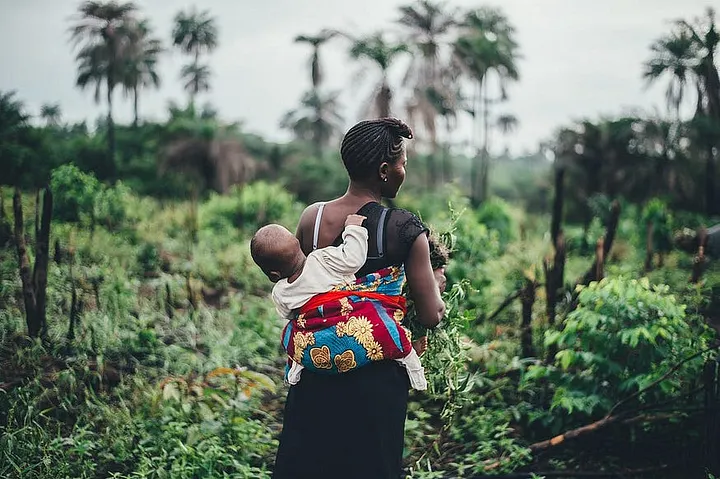 A woman farming with a baby strapped at the back