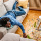 Young black man with hangover sleeping on the sofa in the living room and waking up after the birthday party the night before.