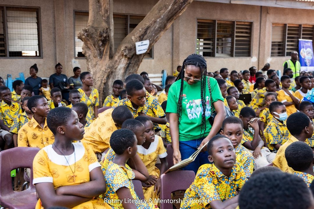 A volunteer with Rotary club assisting the pupils to read a book